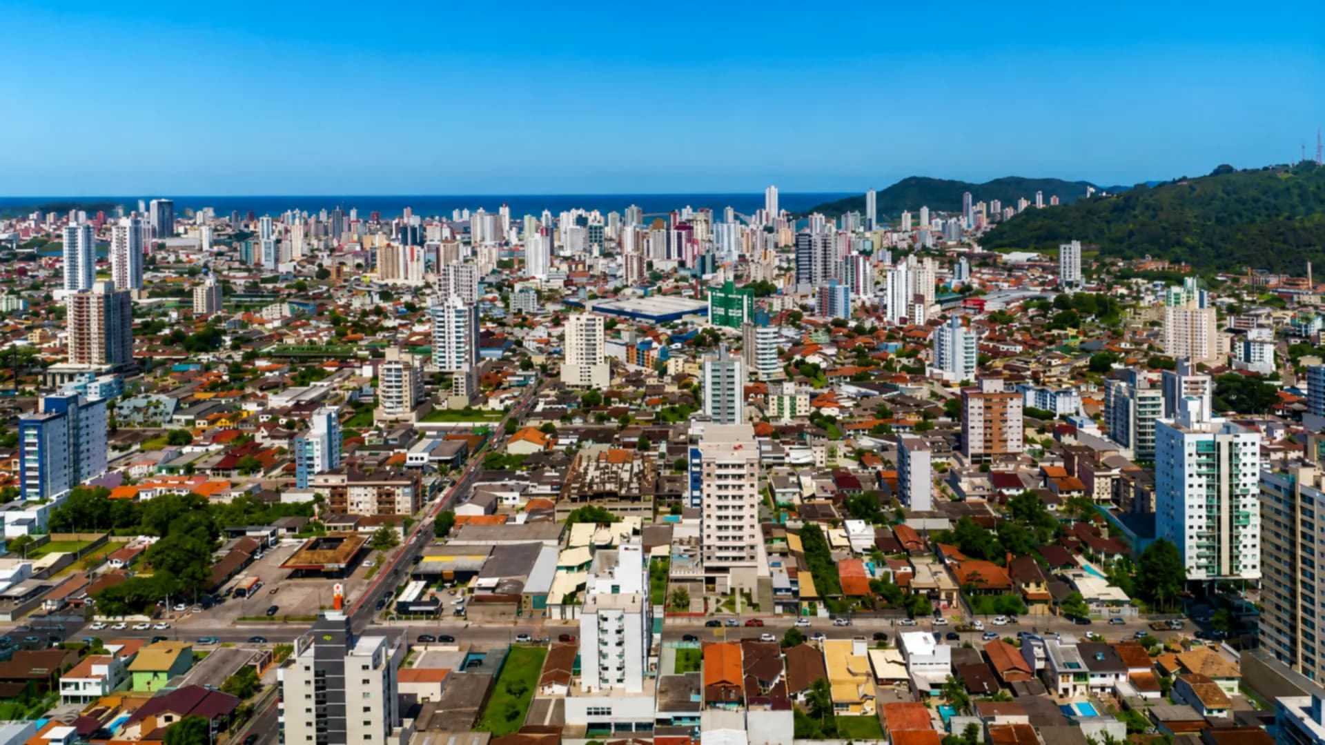 Vista aérea de Itajaí com prédios, morros e o mar ao fundo